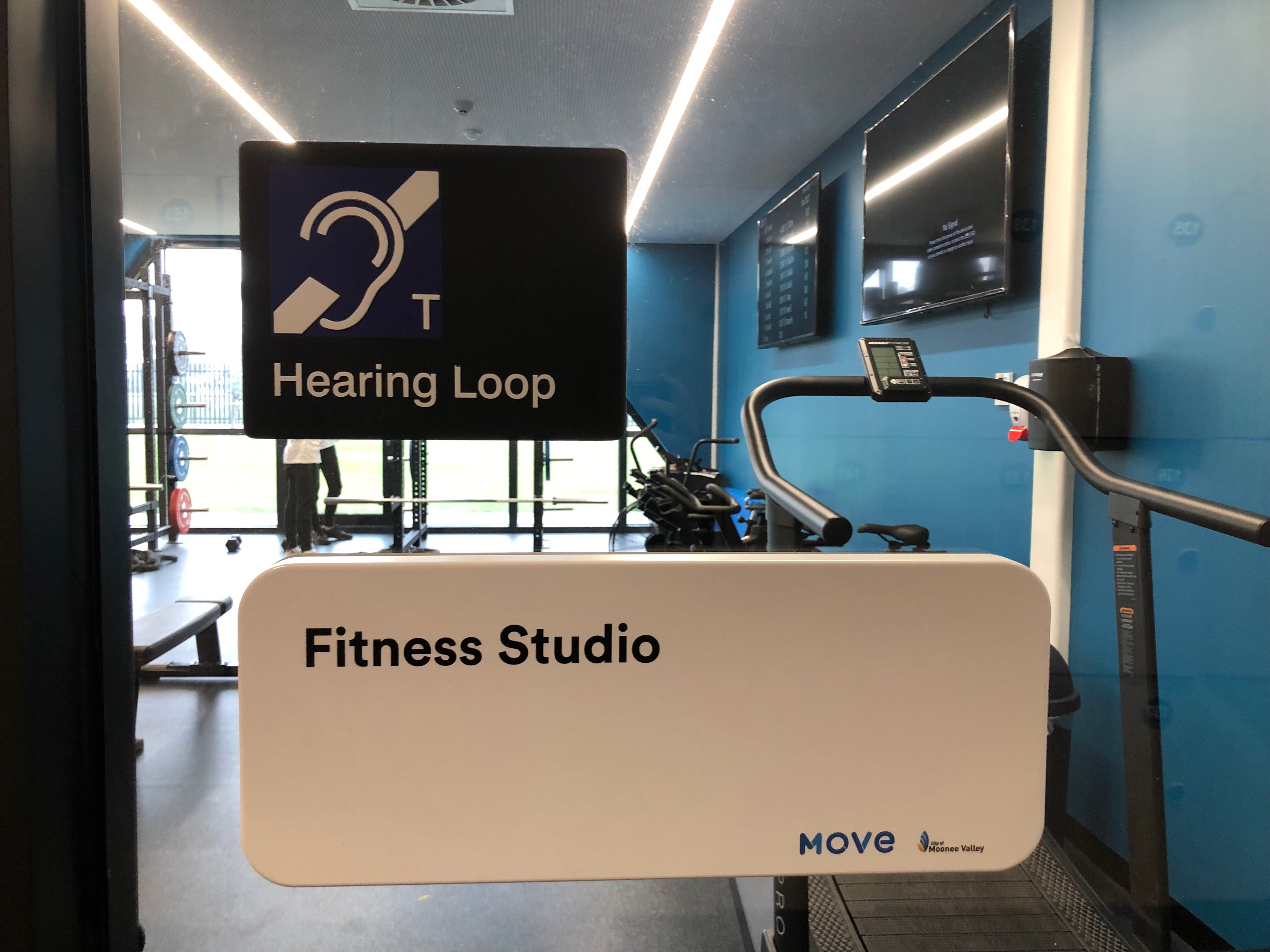 Image of Hearing Loop signage located on a door marked Fitness Studio